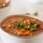 Slow Cooker lentil soup in a grey bowl topped with fresh chopped kale.