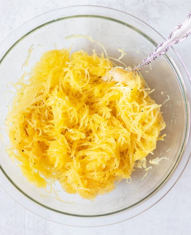 cooked spaghetti squash strands in a clear glass mixing bowl with a fork.