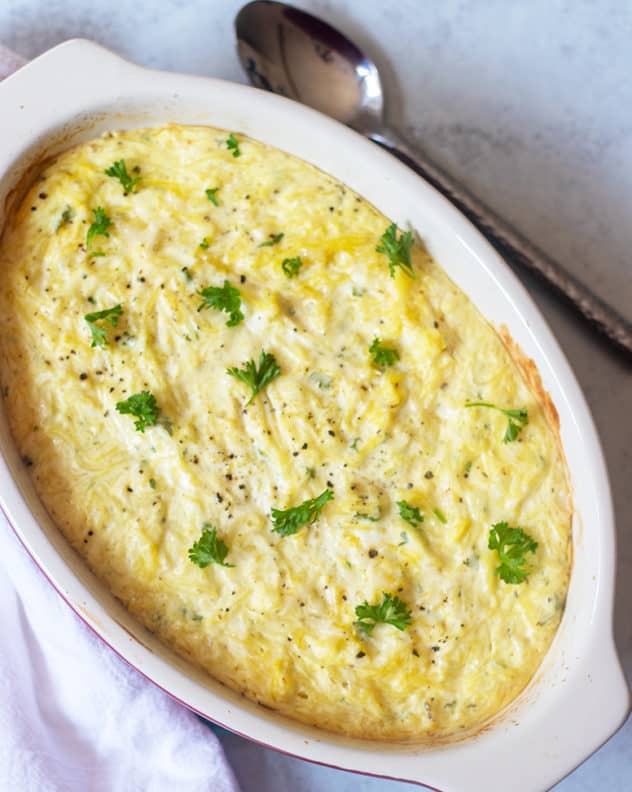 cooked spaghetti squash ricotta in a casserole dish topped with fresh parsley and a serving spoon next to it.