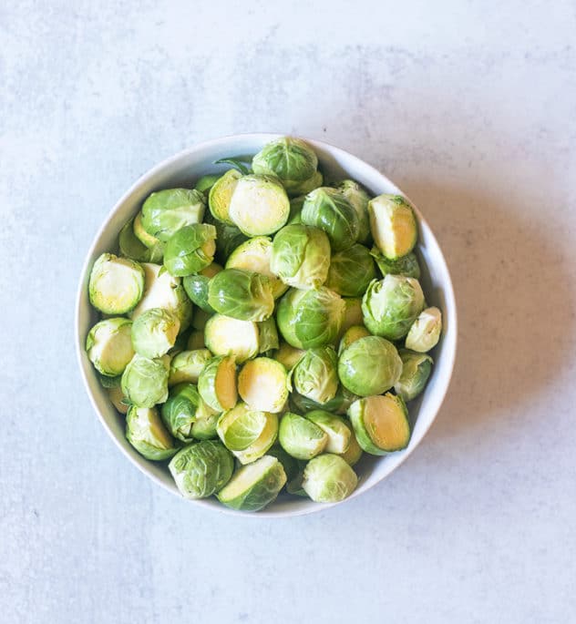 brussel sprouts in a bowl that have been trimmed and sliced in half.