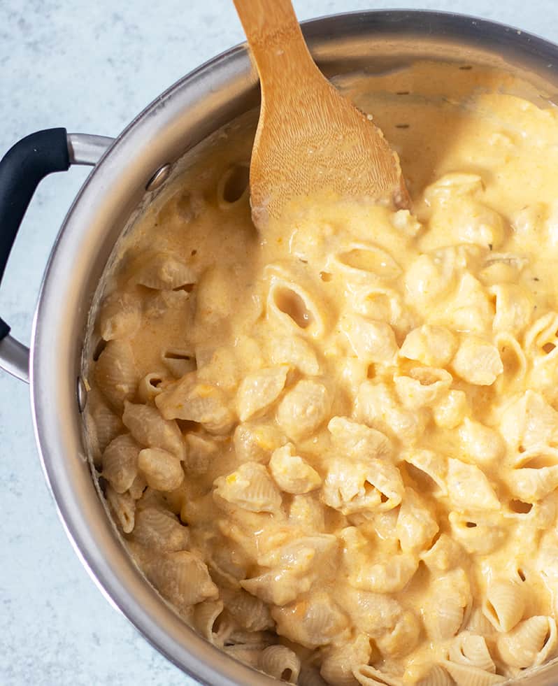 butternut squash Mac and cheese in a sauce pan with a spoon.