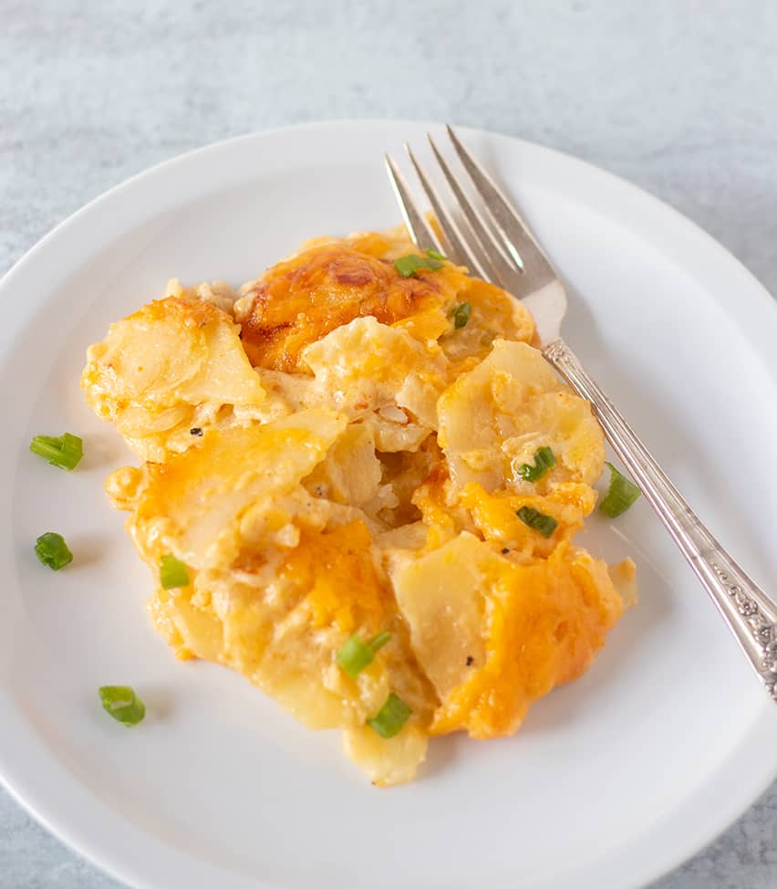 cheesy scalloped potatoes on a plate garnished with green onions.