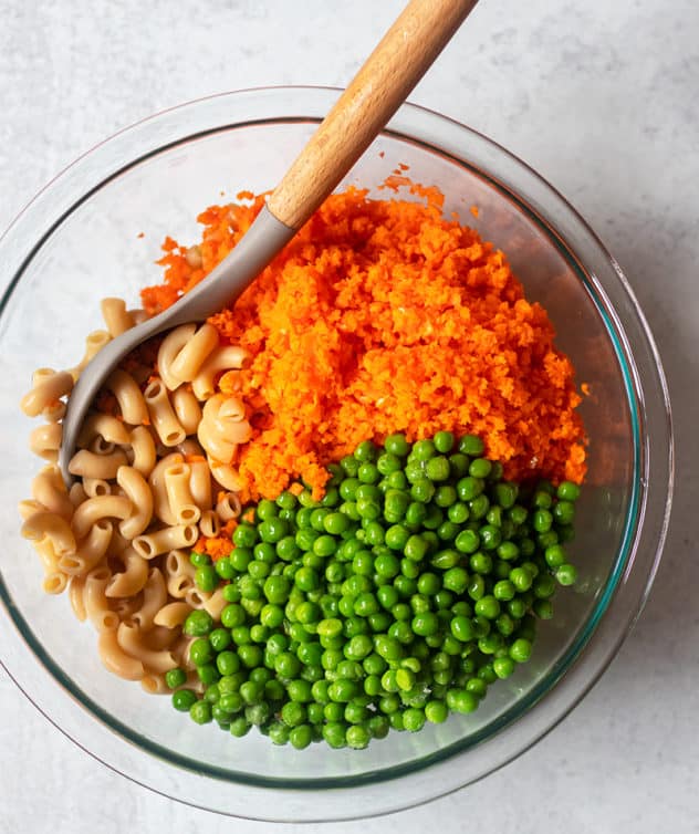 cooked elbow noodles, carrots and peas in mixing bowl
