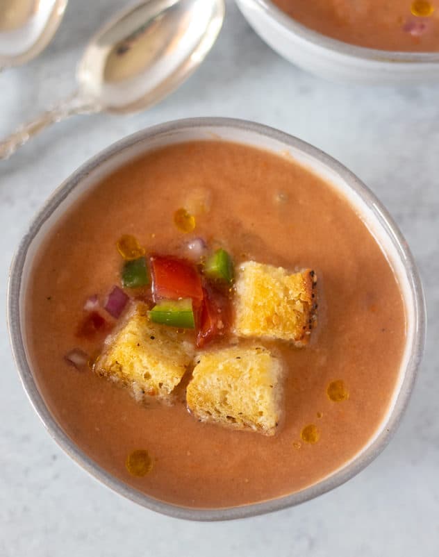 gazpacho soup in a bowl topped with croutons and extra vegetables.