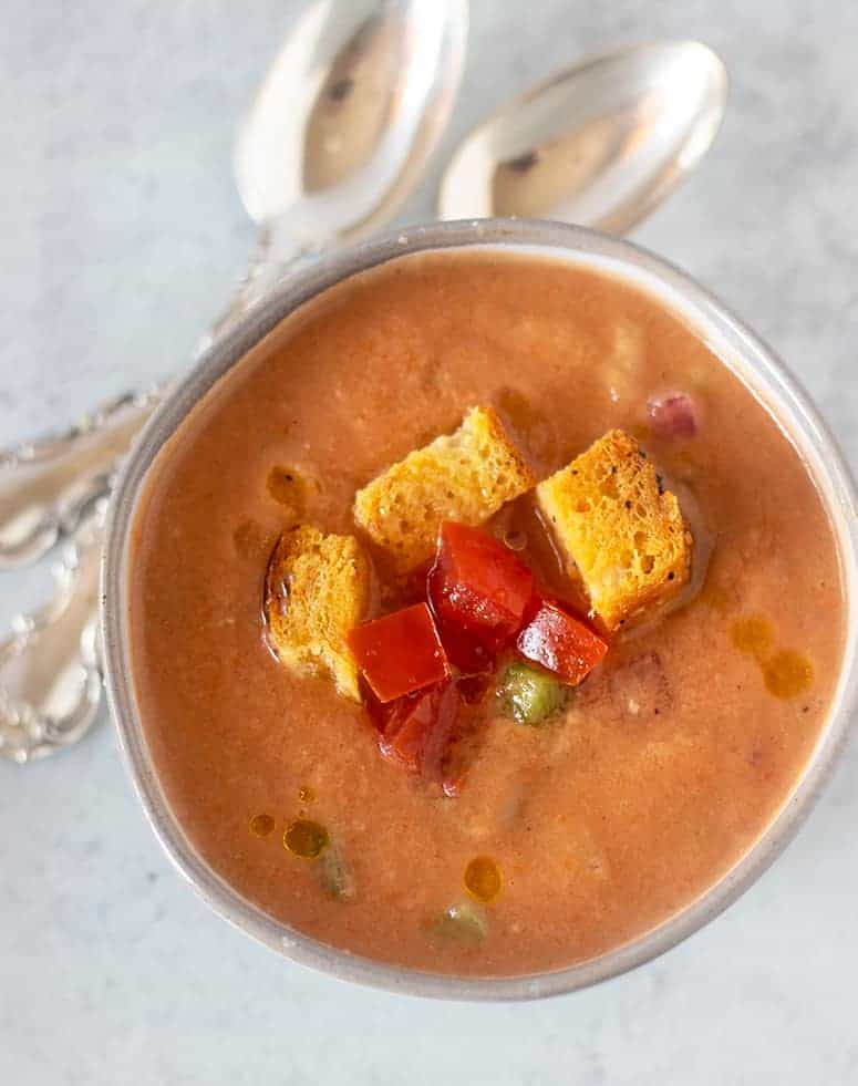Gazpacho soup in a bowl topped with extra veggies and croutons.