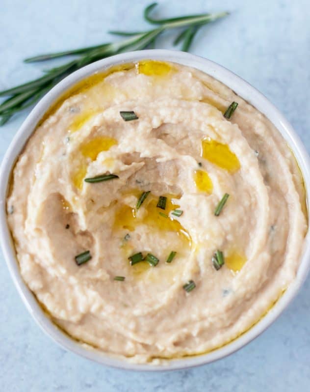 white bean dip in a bowl garnished with fresh rosemary and olive oil