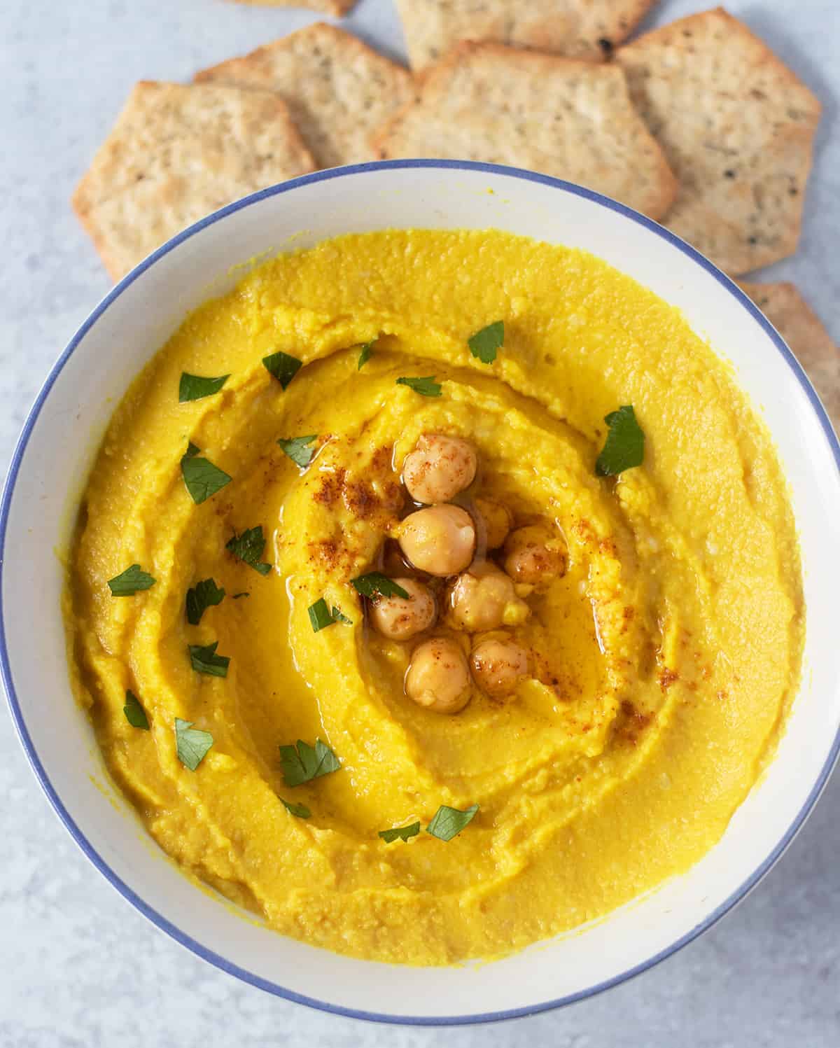 Vegan Turmeric Hummus is a bowl garnished with chickpeas, parsley and olive oil