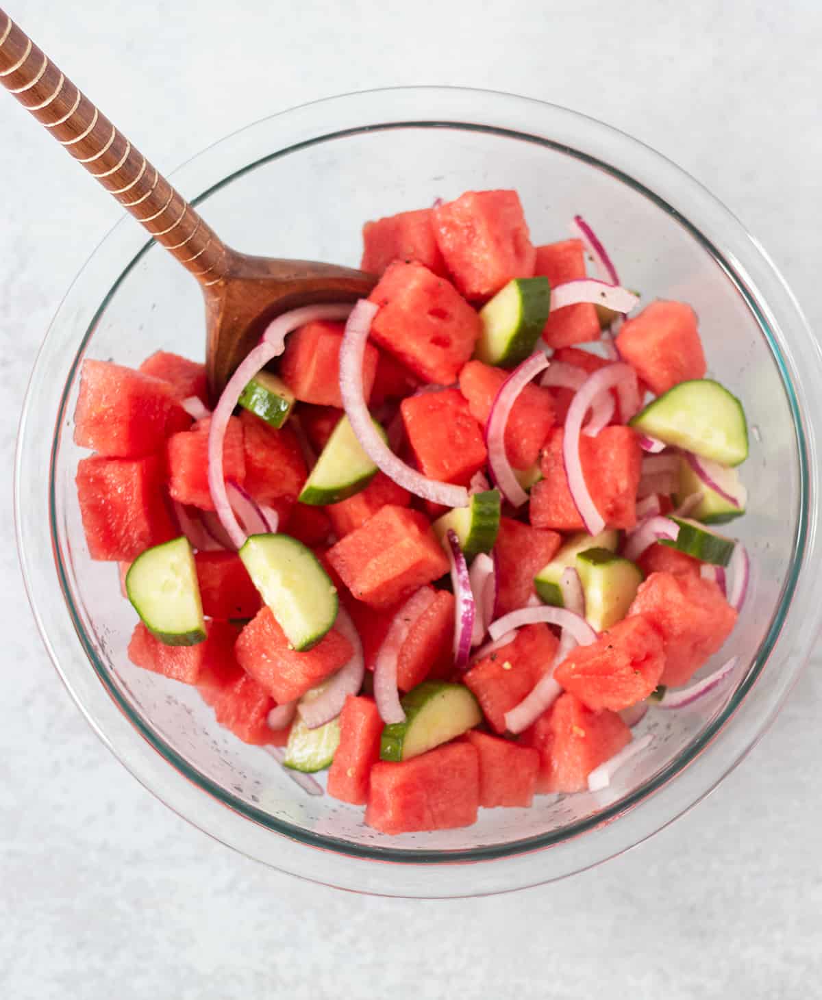 watermelon, cucumber, red onion in clear glass mixing bowl.