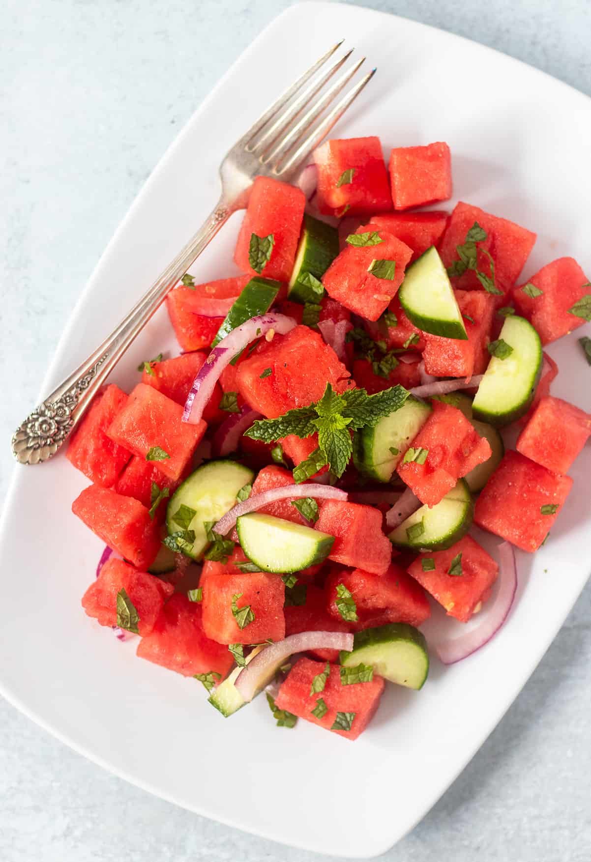 watermelon cucumber salad on white serving plate with a silver fork.