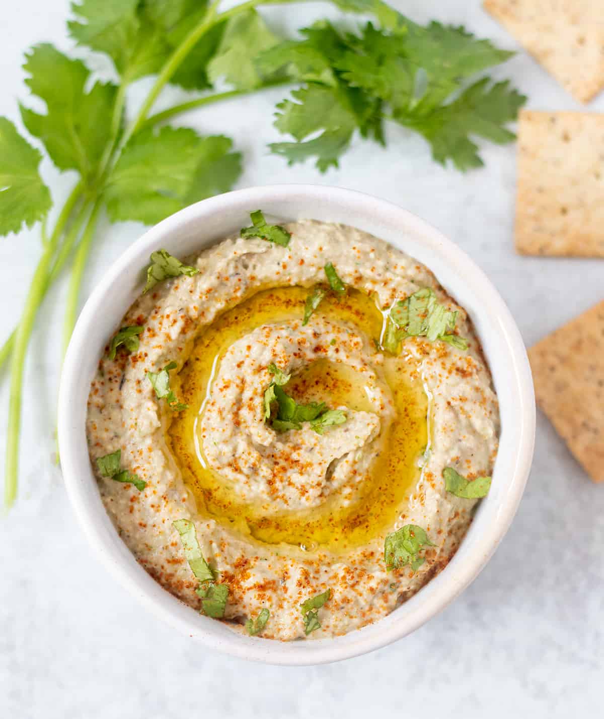 hummus in a bowl topped with olive oil, cilantro and paprika