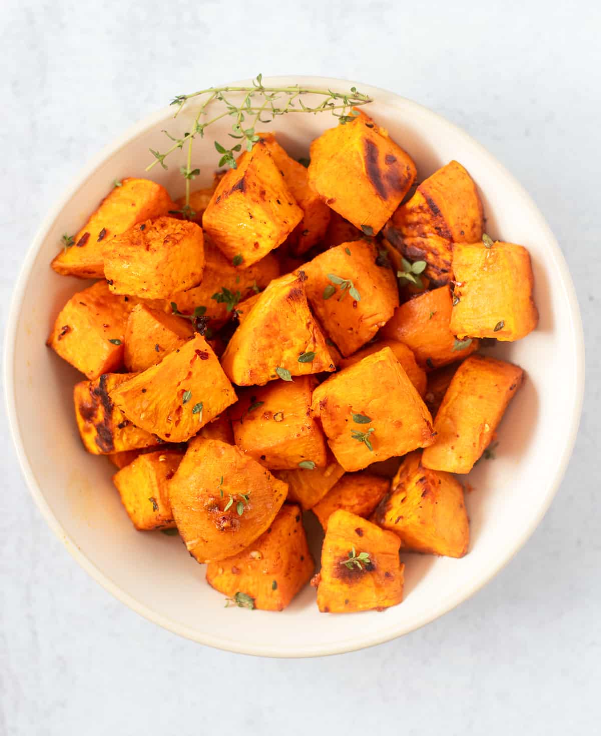 roasted sweet potato cubes in a white serving bowl with fresh thyme