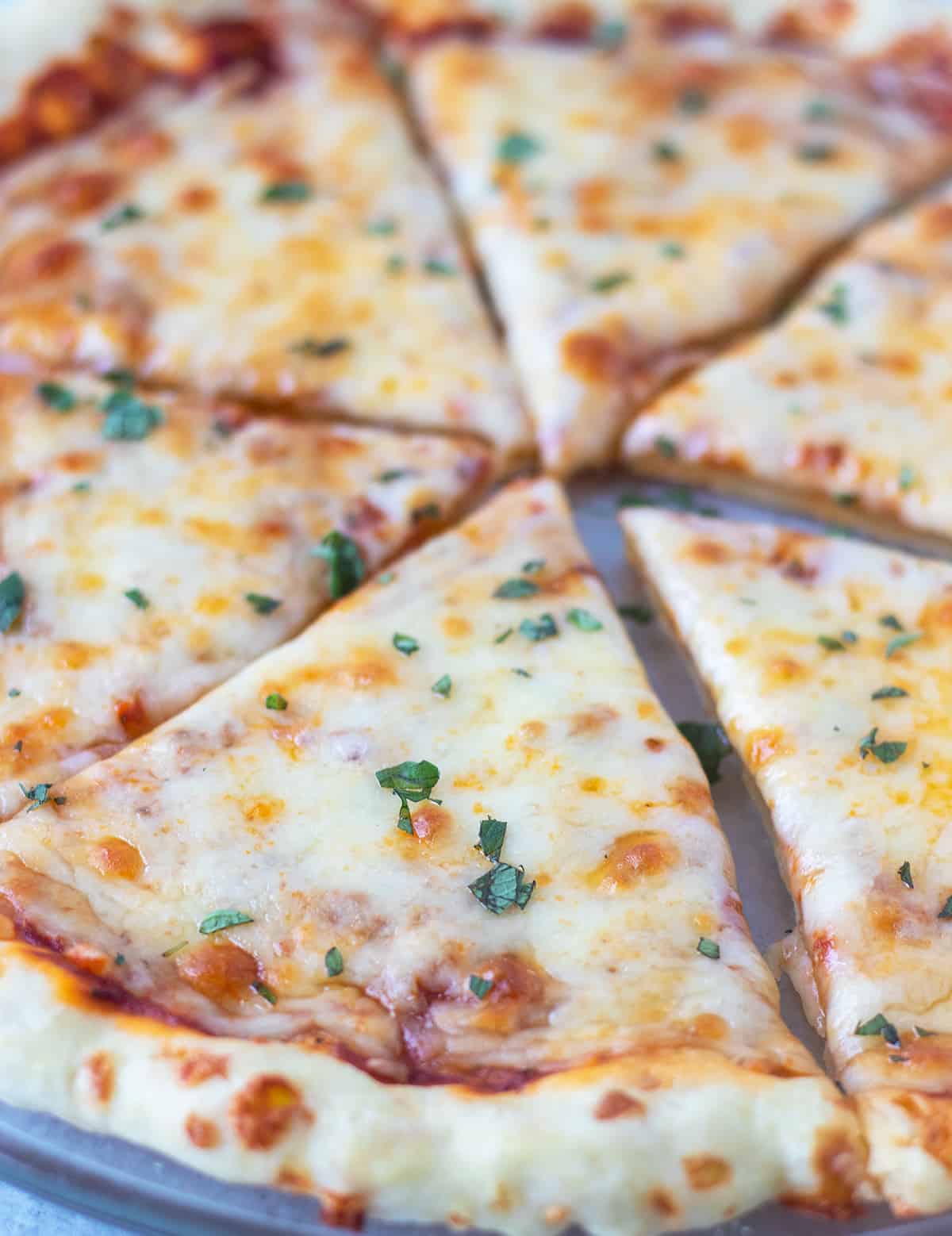 cheese pizza sliced and on a glass serving plate topped with fresh oregano.