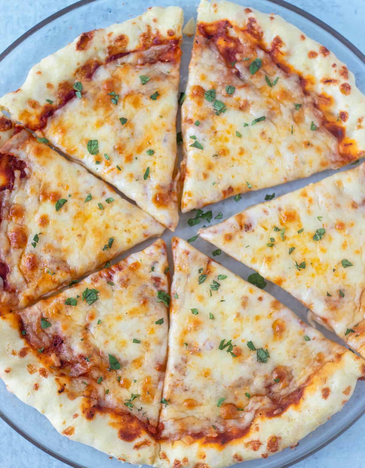 Cooked topped gluten free pizza crust cut and on a serving plate with fresh oregano