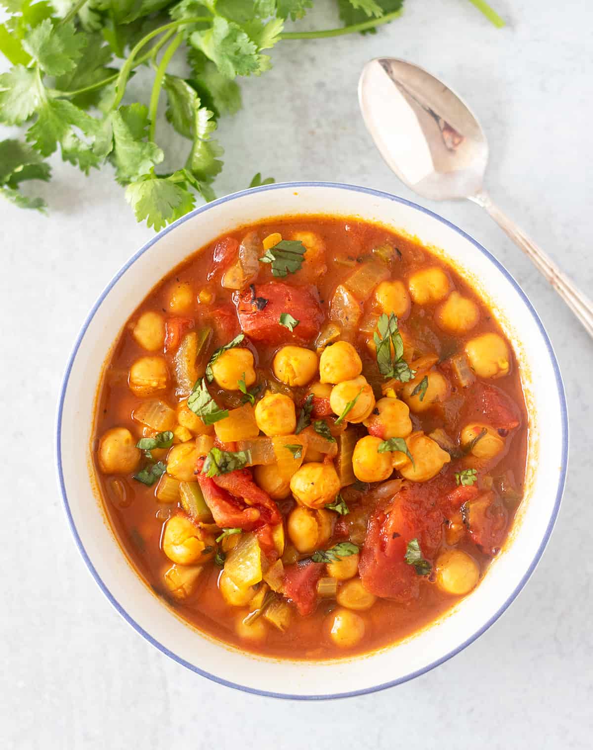 Masala Chickpea Soup in a white bowl garnished with cilantro and a silver spoon next to the bowl