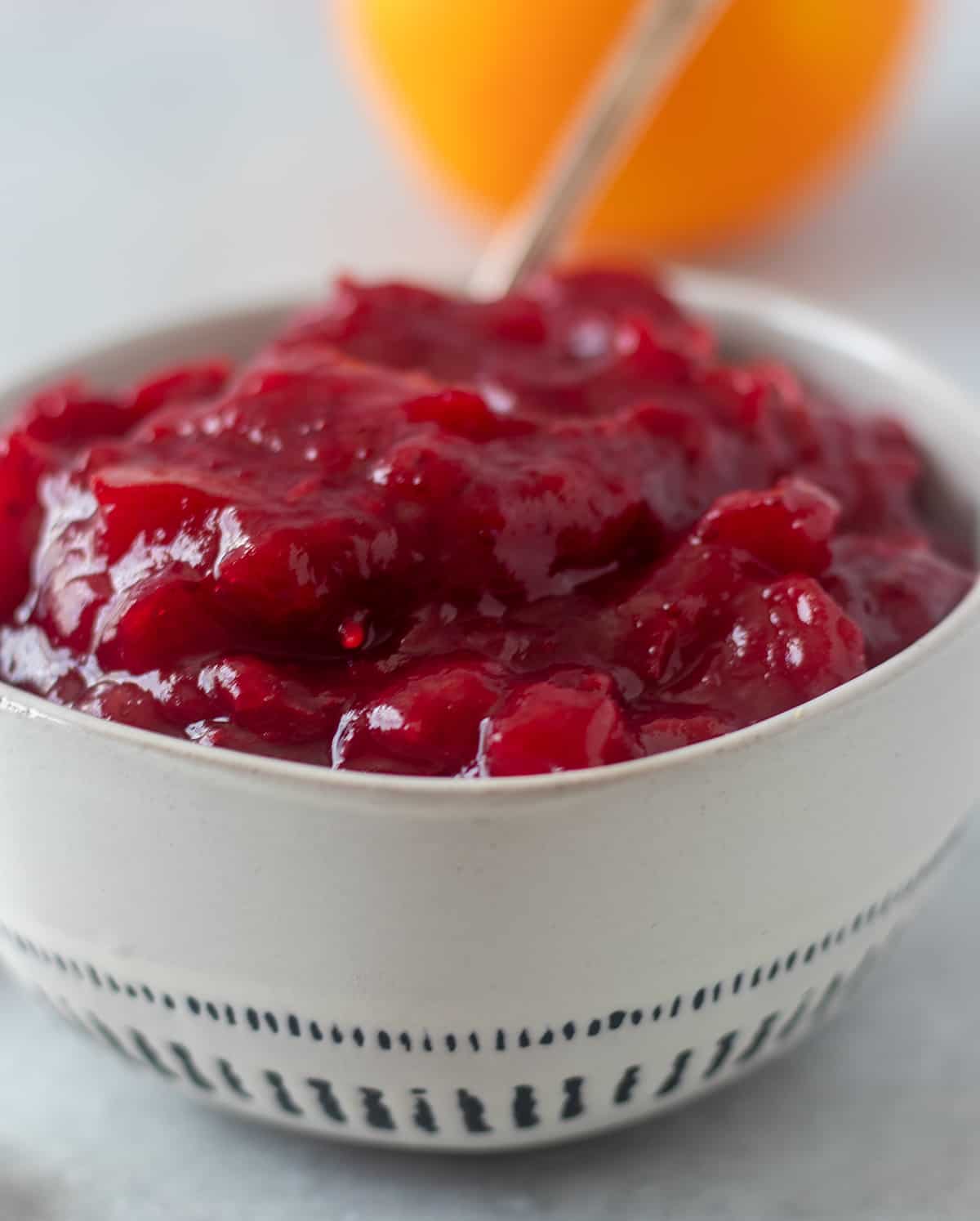 cranberry sauce in a white bowl with a silver spoon and an orange in the background