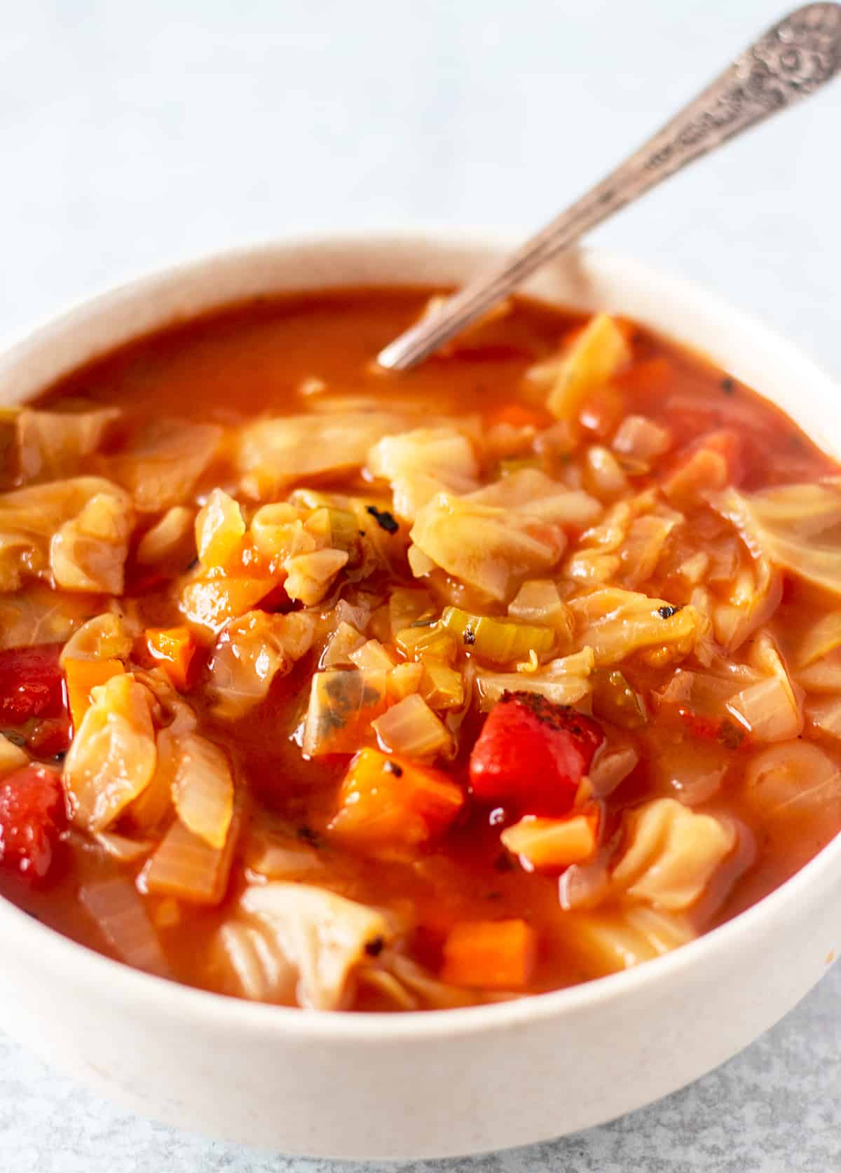 cabbage soup in a white serving bowl with a silver spoon