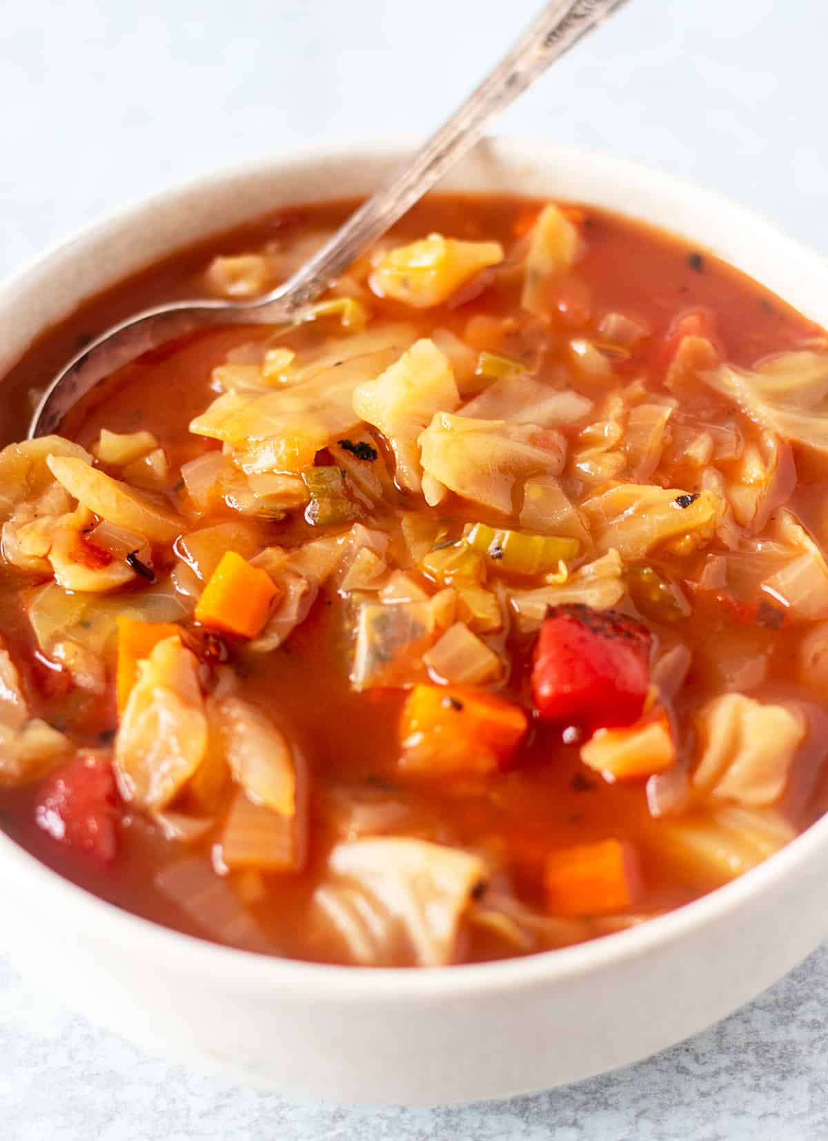 Cabbage soup in a white bowl with a silver serving spoon