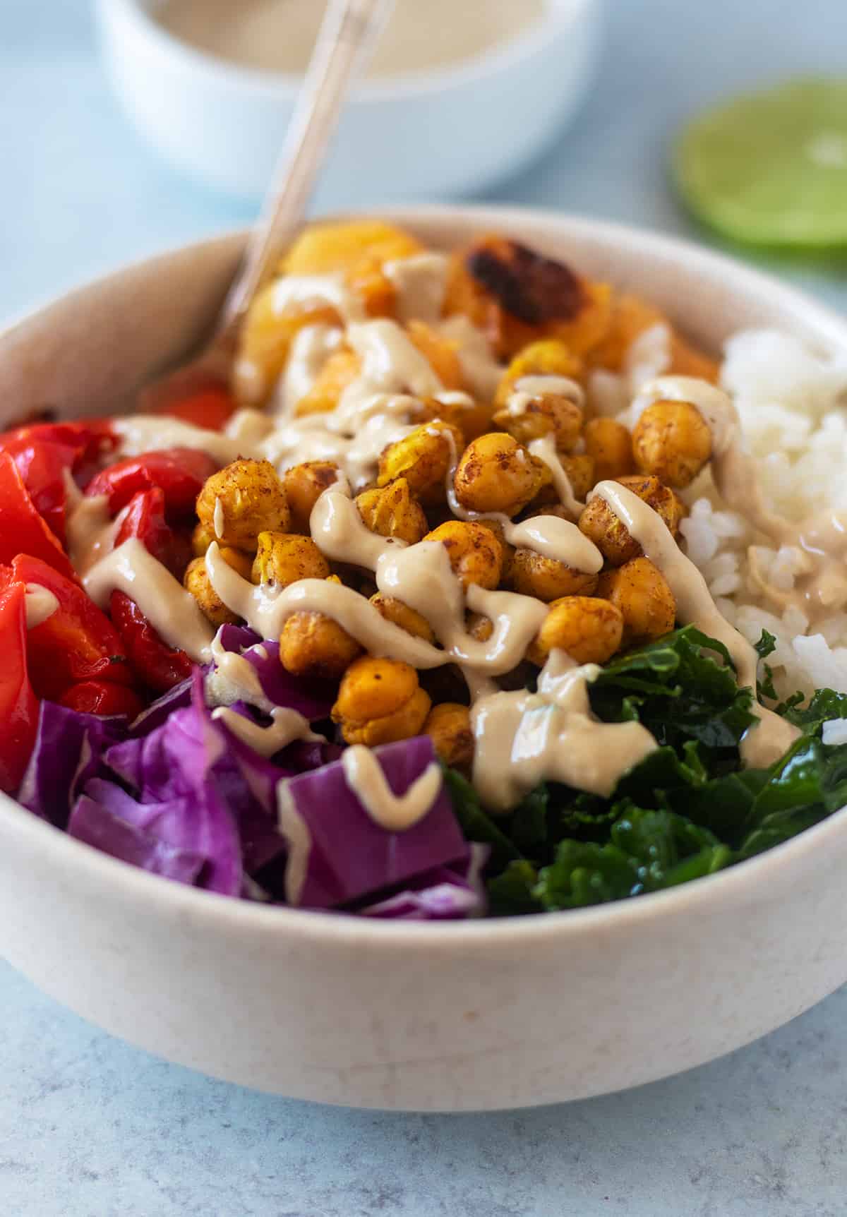 buddha bowl in a white bowl with silver spoon that's topped with tahini sauce