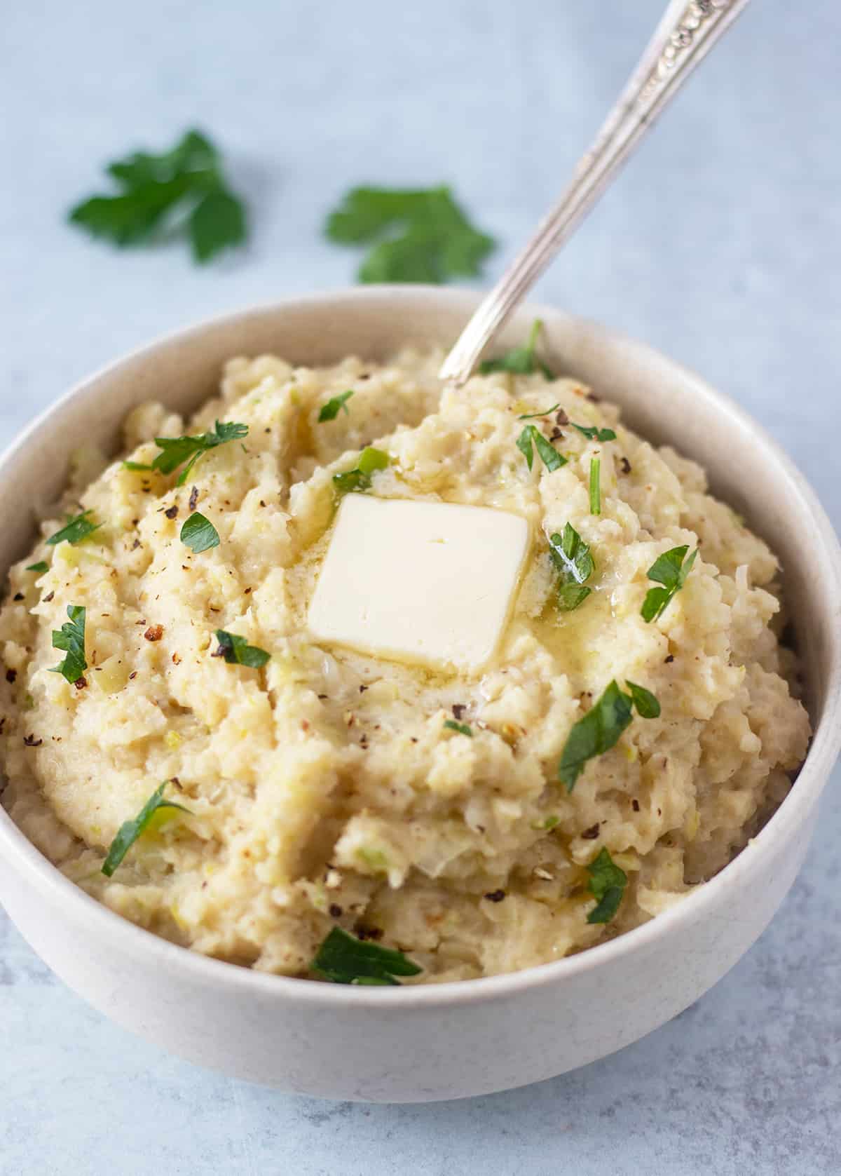 mashed colcannon in a white bowl with garnished with chopped parsley, black pepper and melty butter