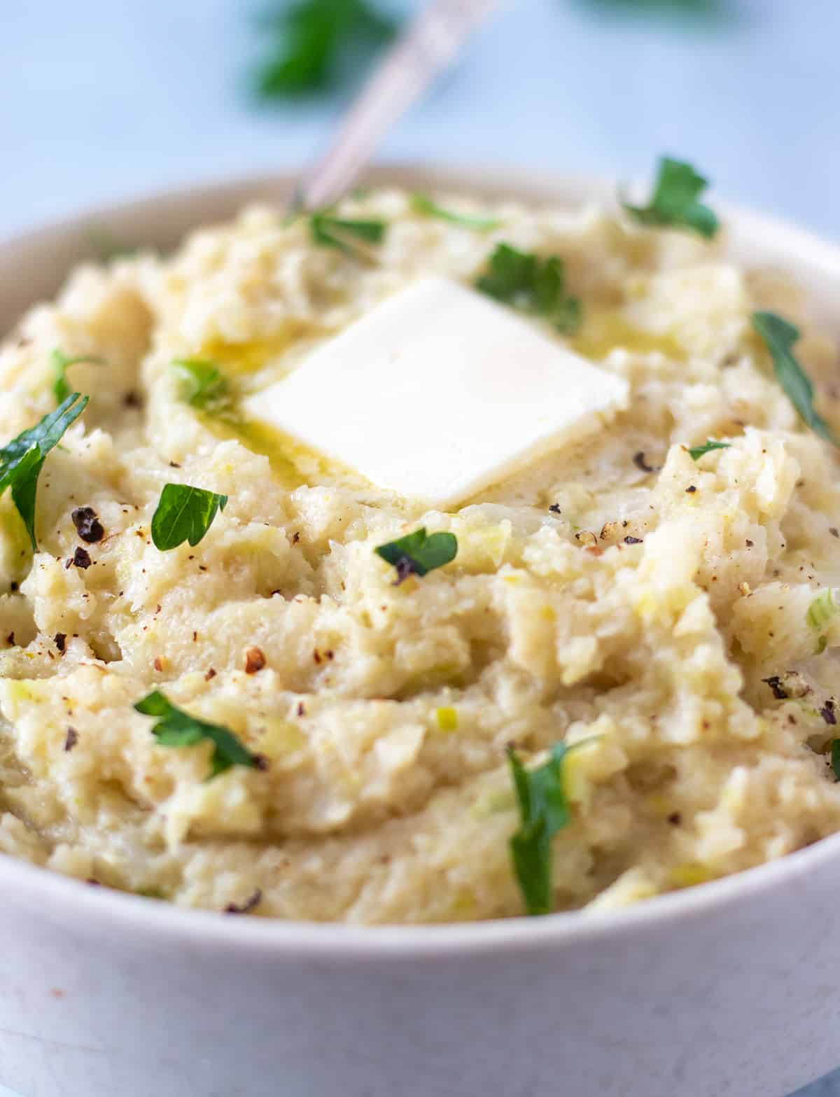 cooked mash in a white bowl with chopped parsley and butter