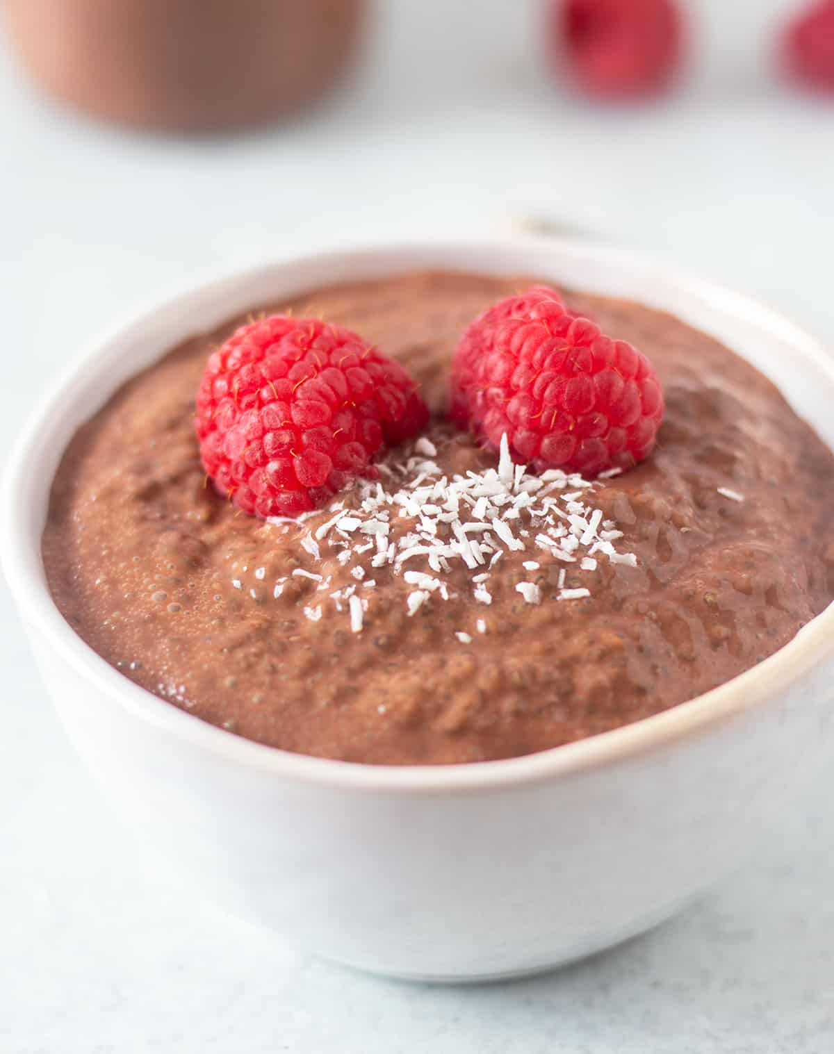 chocolate chia seed pudding in a white bowl topped with fresh raspberries and shredded coconut