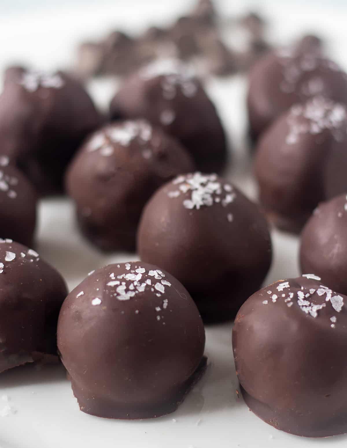 dark chocolate truffles on a white plate topped with flaky sea salt