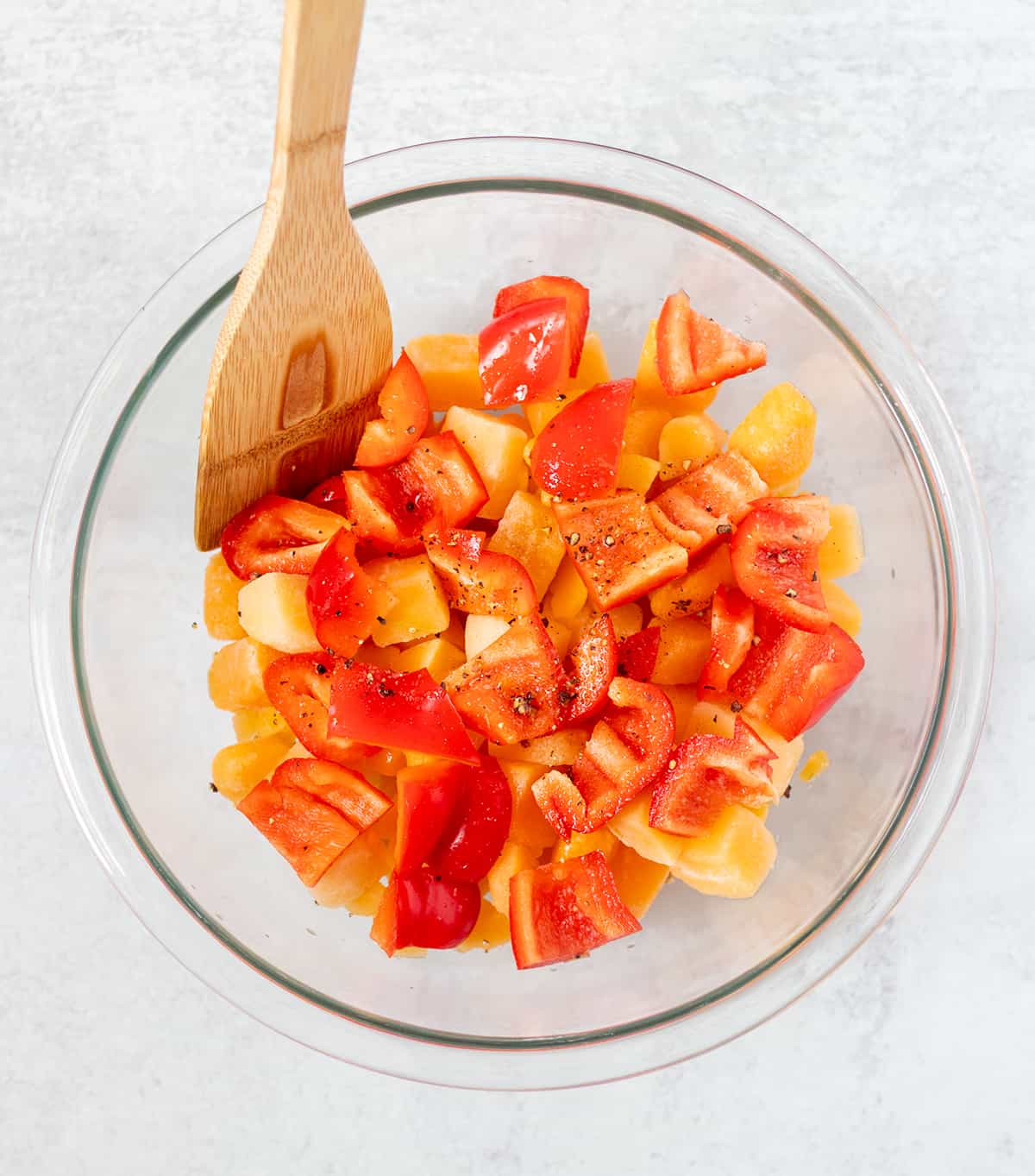 butternut squash and red pepper chunks in a clear glass serving bowl with olive oil, salt and pepper