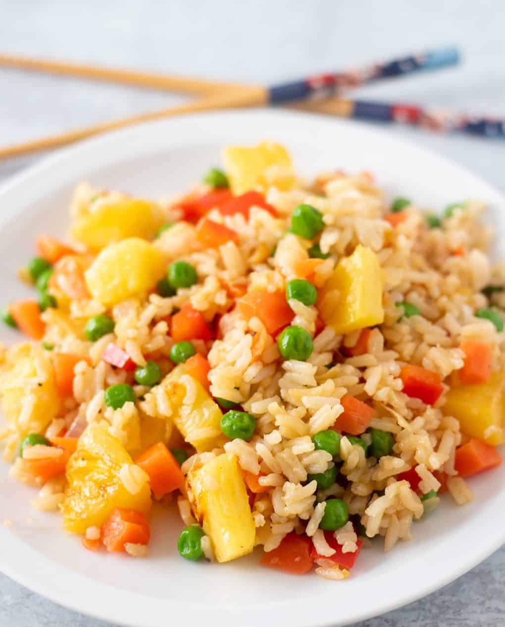pineapple fried rice on a white plate with chopsticks beside the plate for serving.