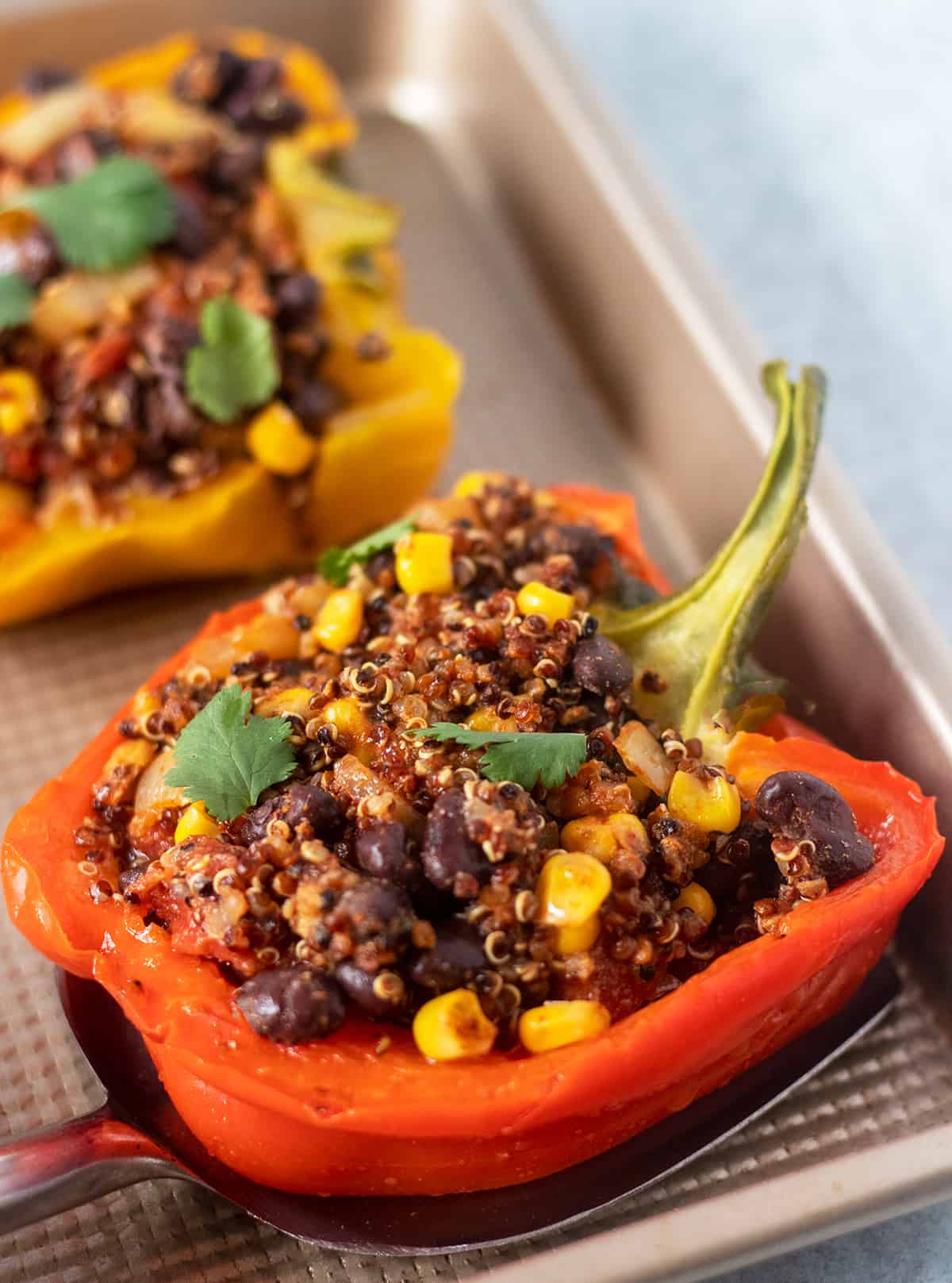 Vegan stuffed peppers on a gold baking pan with a spatula underneath one