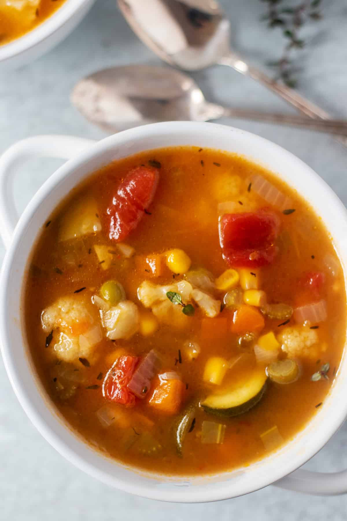 vegetable soup in a white bowl with two silver spoons in background and fresh thyme