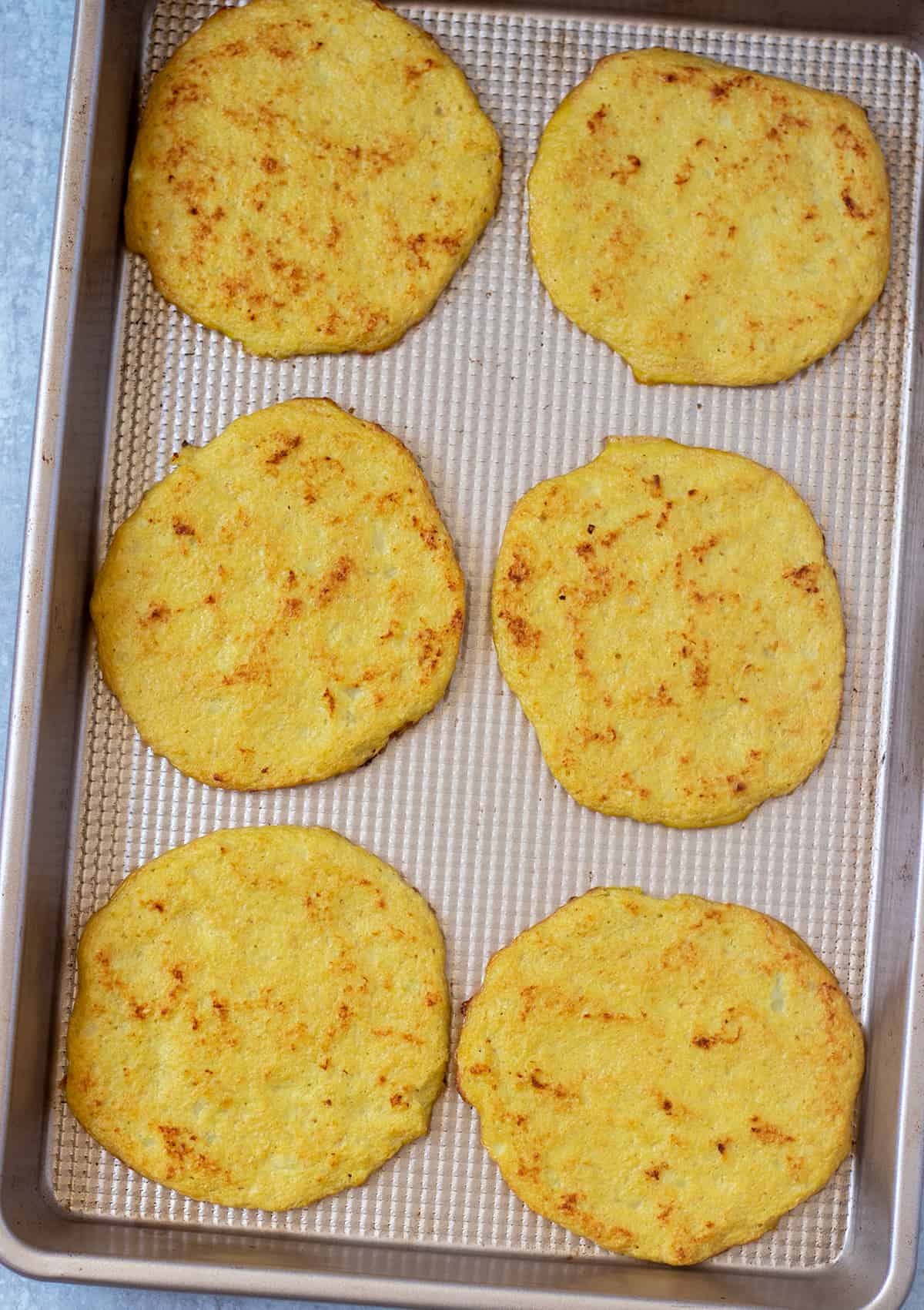 cauliflower tortillas on a gold baking pan after cooking.
