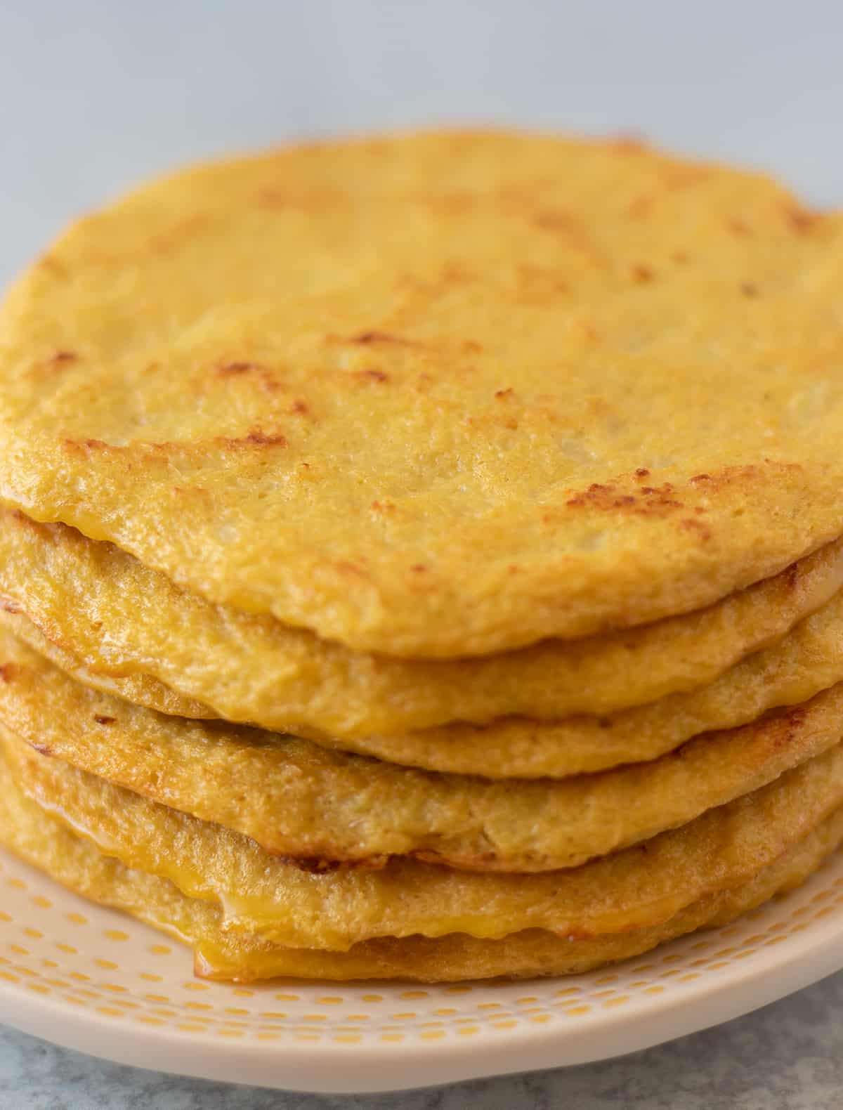 cauliflower tortillas stacked on a white plate with yellow trim