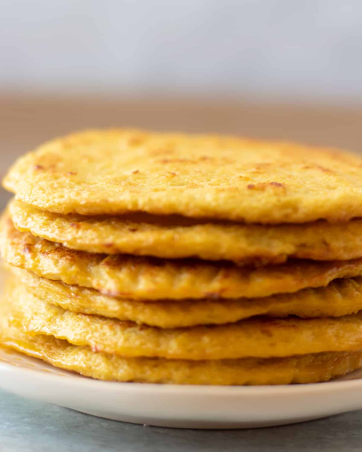 cauliflower tortillas stacked on a white plate with yellow trim