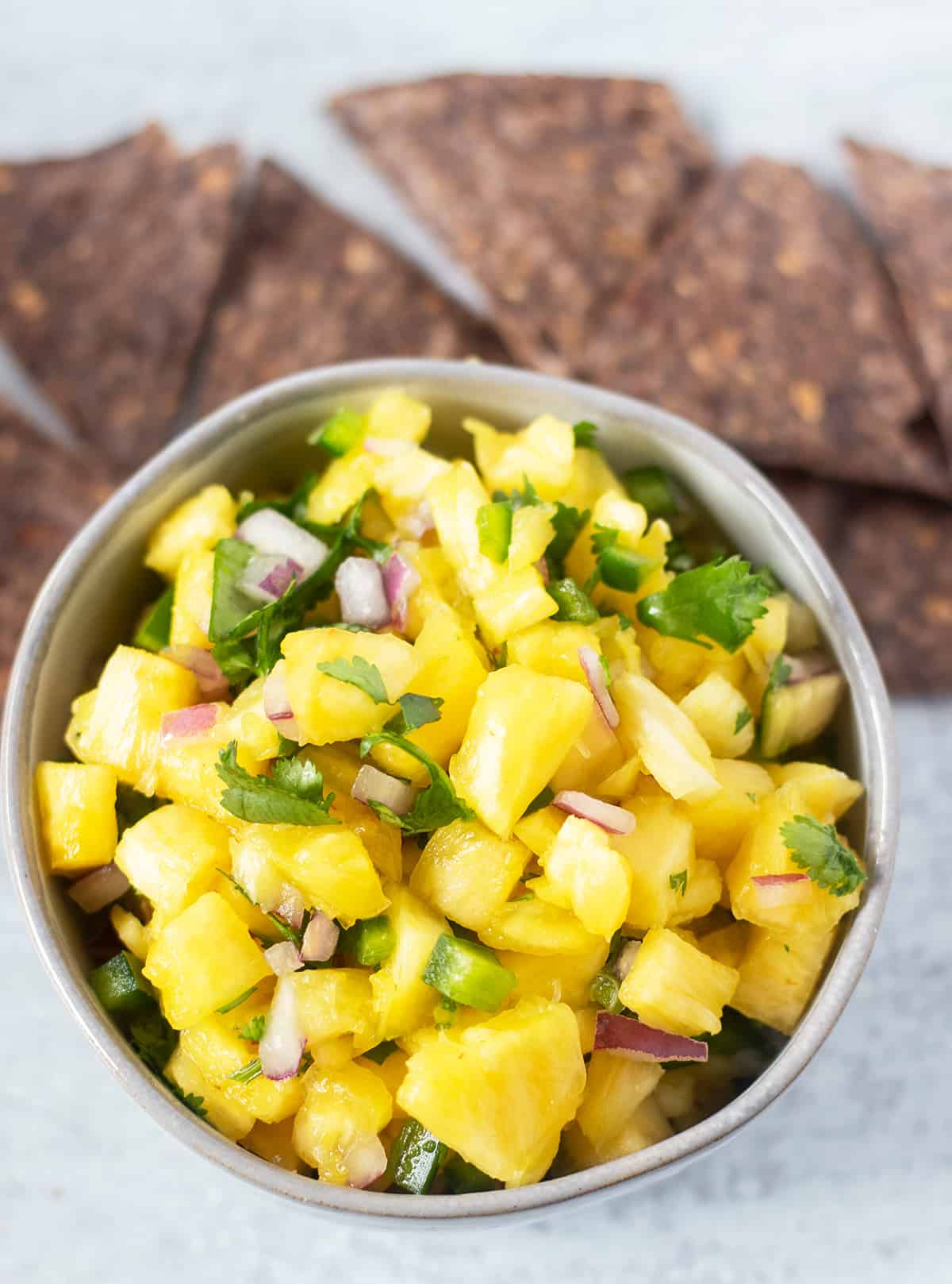 pineapple salsa in a grey bowl with blue tortilla chips beside the bowl for serving.