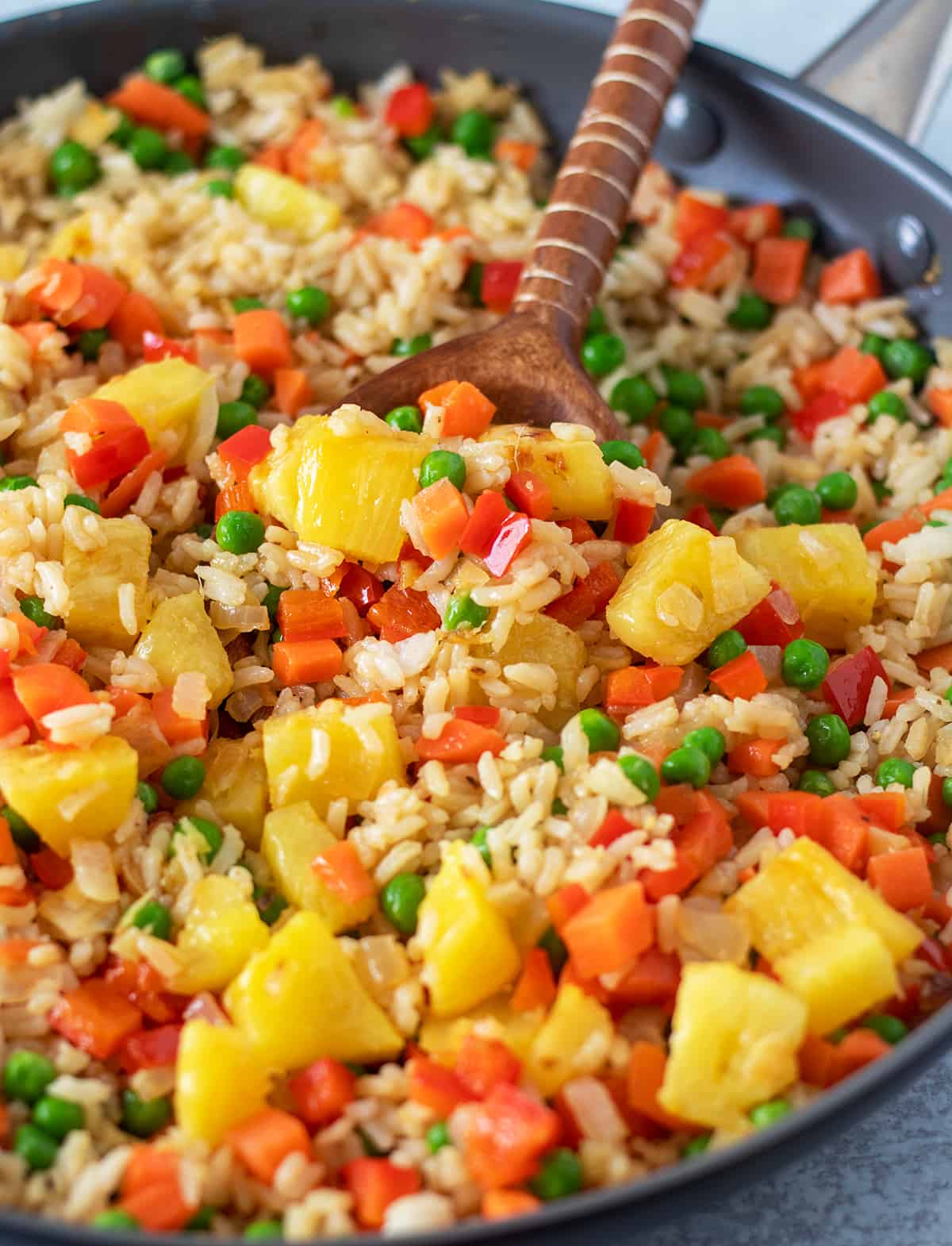 pineapple fried rice in a sauté  pan with a wooden spoon