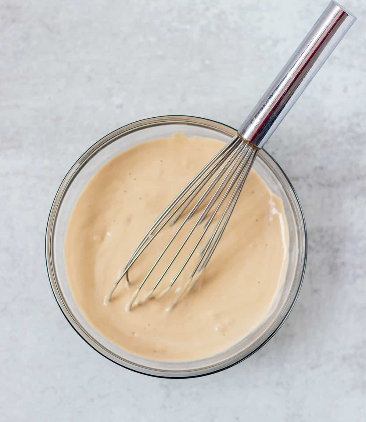 tahini dressing in a clear glass mixing bowl with a silver whisk.