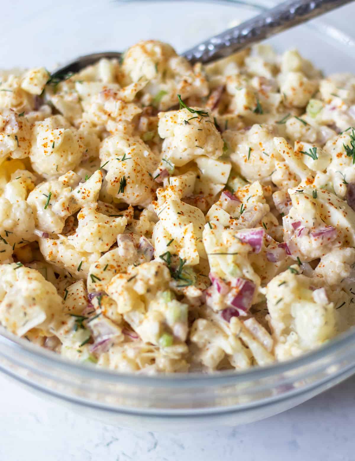 cauliflower potato salad in a clear glass bowl with a silver fork for serving.