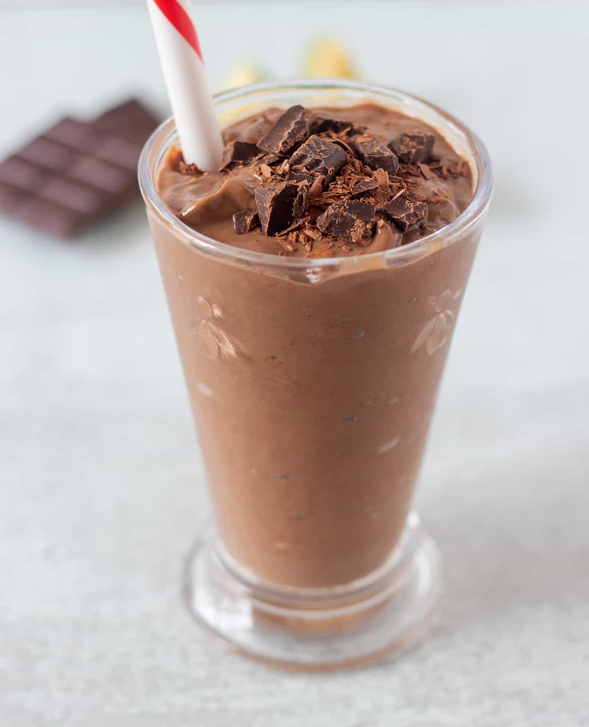 chocolate avocado smoothie in a clear glass topped with chopped chocolate and a red and white straw in the glass for serving.