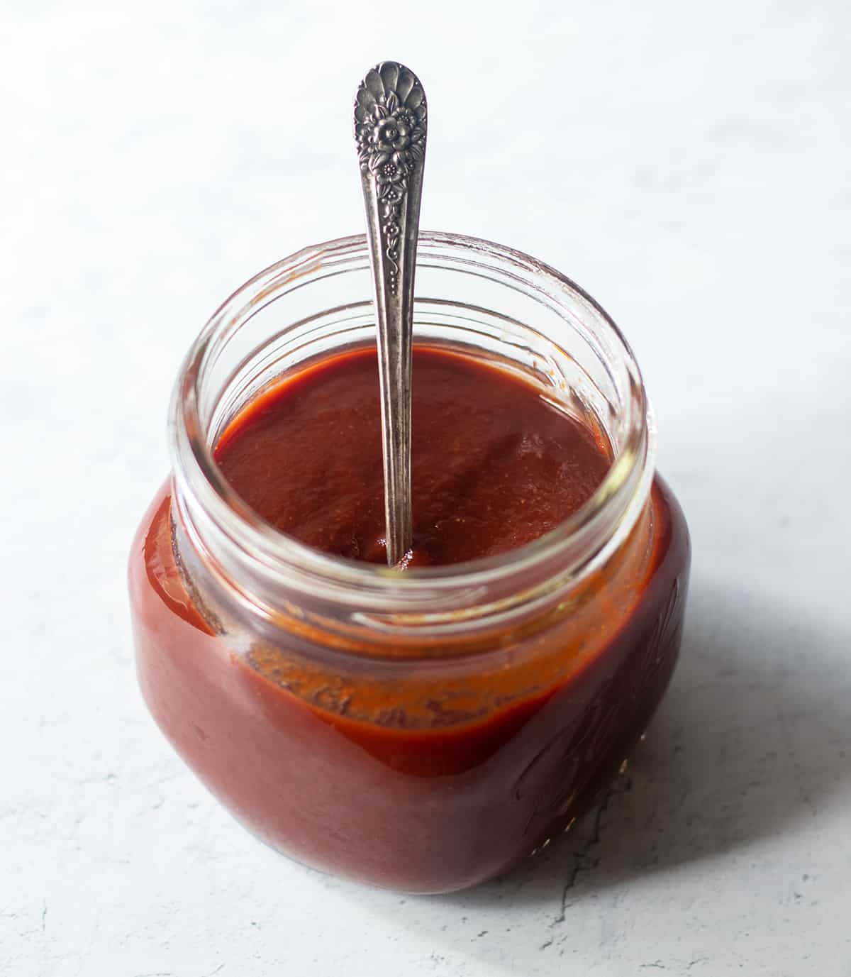 Homemade barbecue sauce in a clear glass jar with a silver spoon