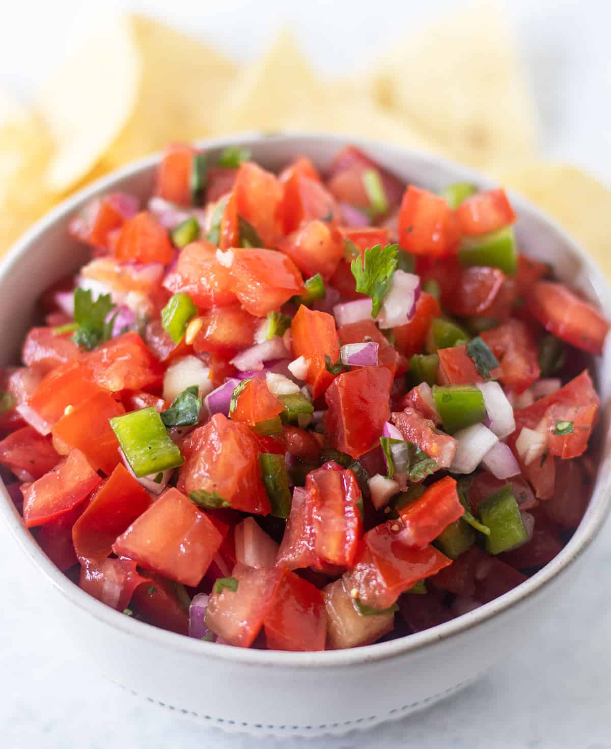 pico de gallo in a white bowl with blue trim and tortilla chips are beside the bowl.