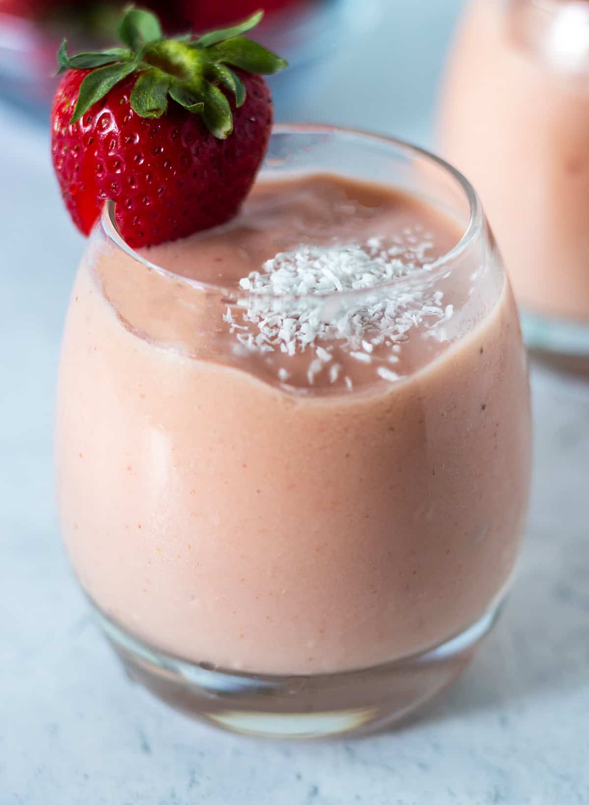 tropical smoothie in a clear glass garnished with shredded coconut and a fresh strawberry on the side of the glass.
