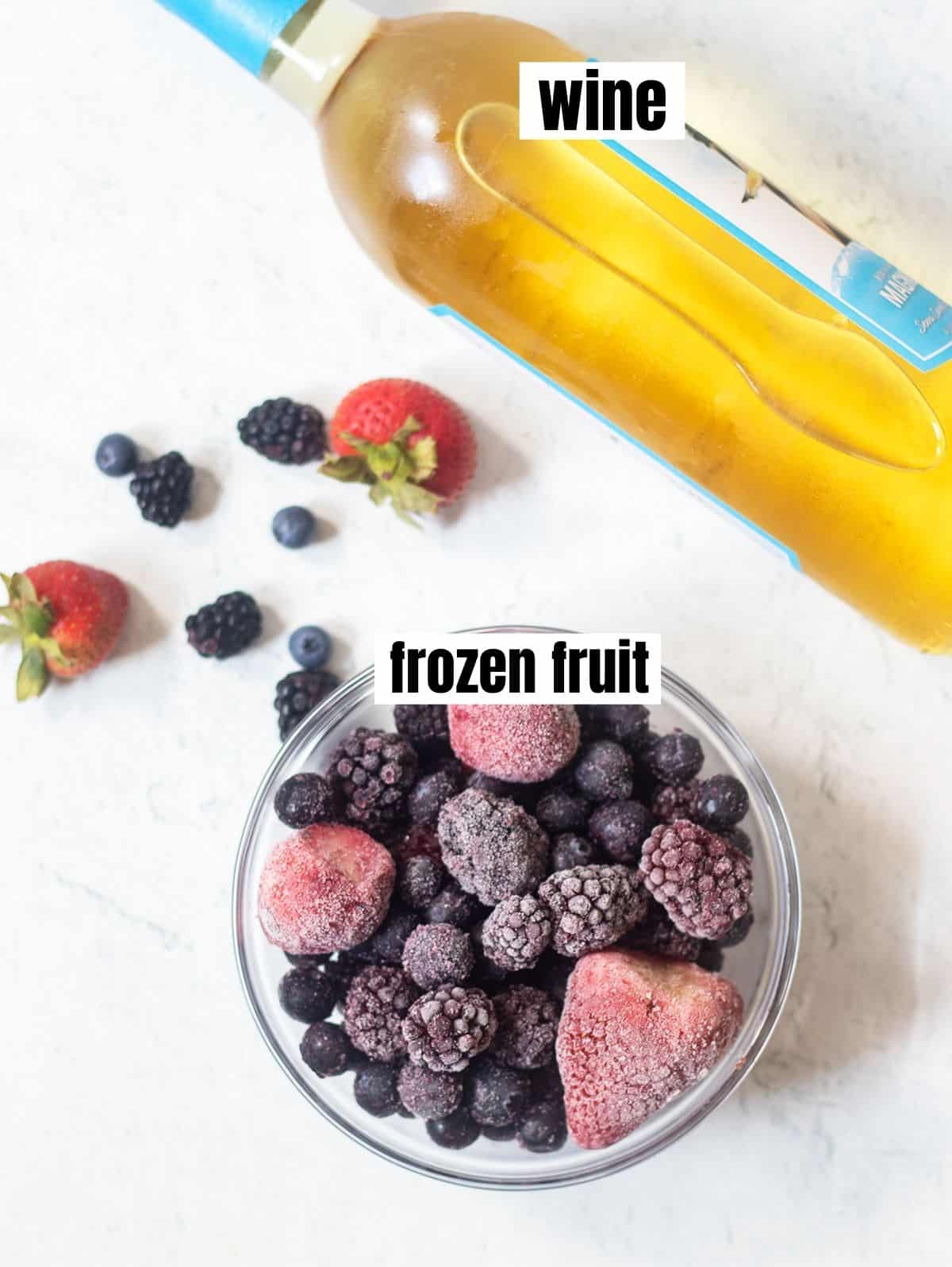 bottle of white wine and a blend of frozen blackberries, blueberries and strawberries in a bowl. Some fresh strawberries, blueberries and blackberries in the background.