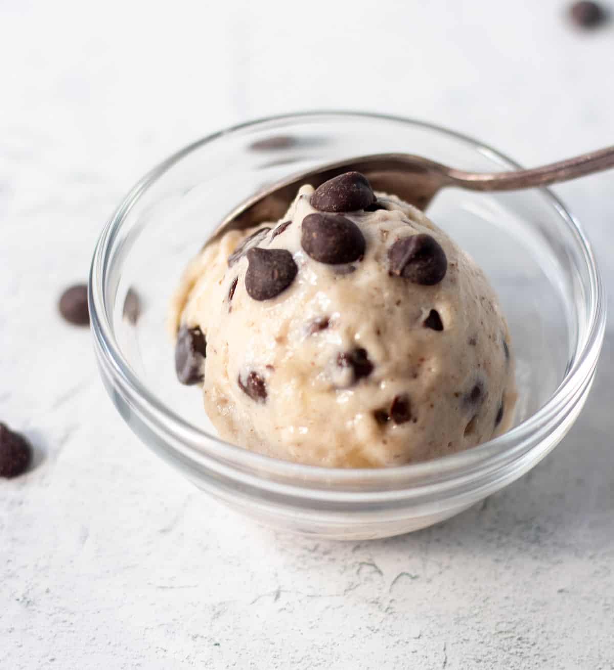 mint chocolate chip nice cream in a clear glass bowl topped with extra chocolate chips and a silver spoon in the bowl.