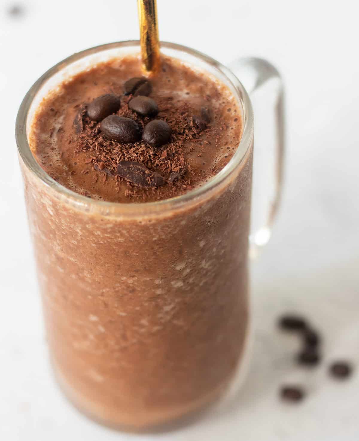 mocha coffee smoothie in a clear glass topped with shaved chocolate and coffee beans.