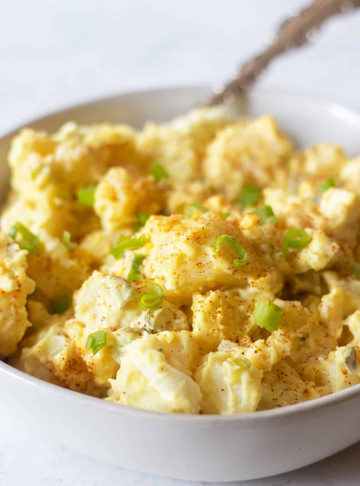 mustard potato salad in a white bowl garnished with paprika and green onions. 