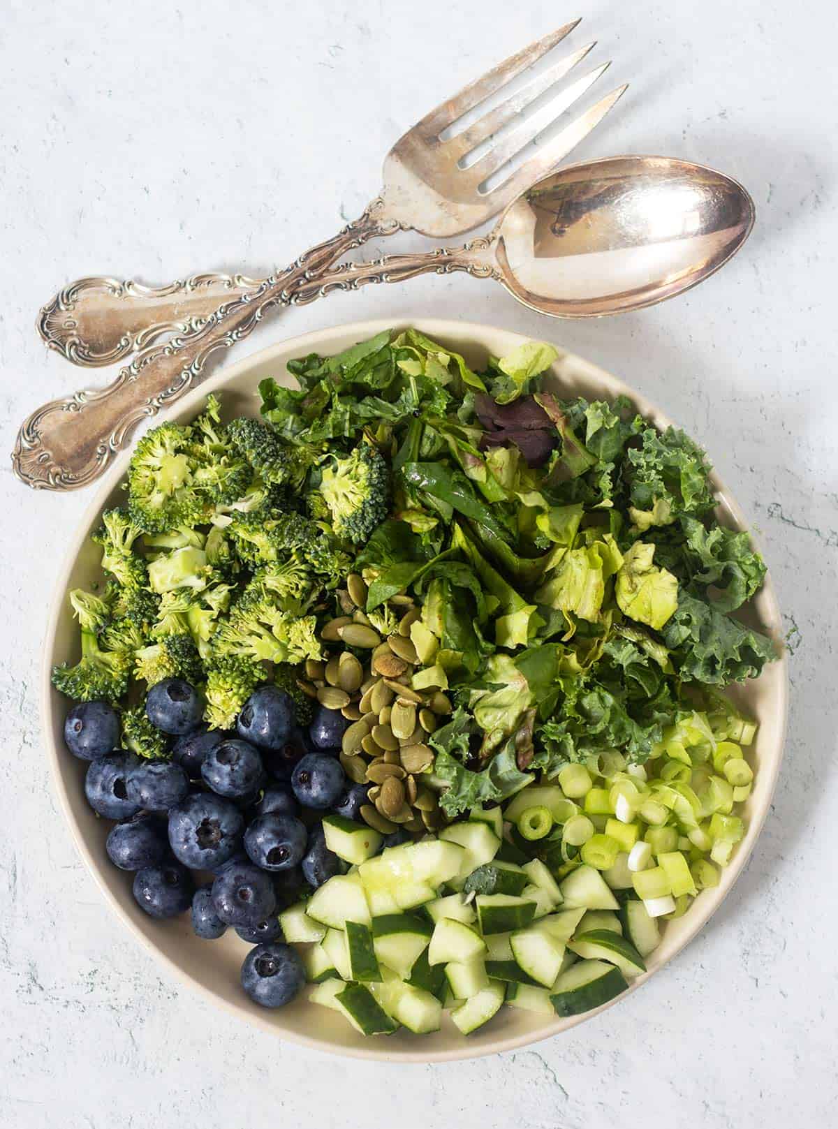 superfood salad on a white salad plate with silver salad fork and spoon for serving.