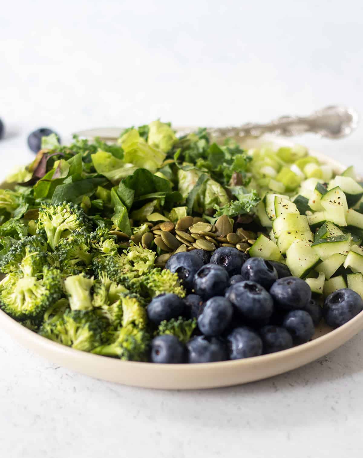 superfood salad on a white salad plate garnished with freshly cracked black pepper and a silver fork for serving.