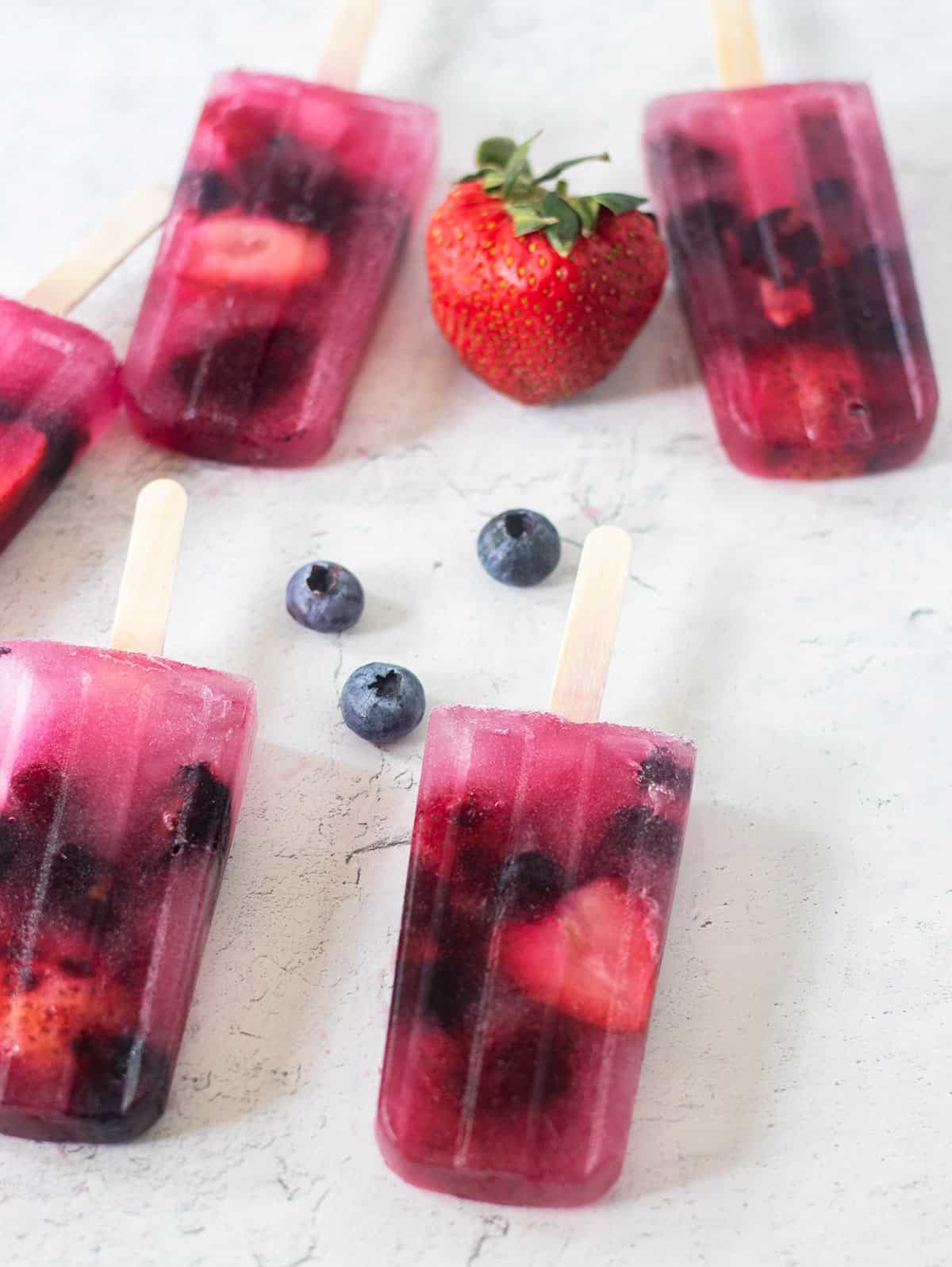 mixed fruit berry popsicles on a white board with a fresh strawberry and fresh blueberries.