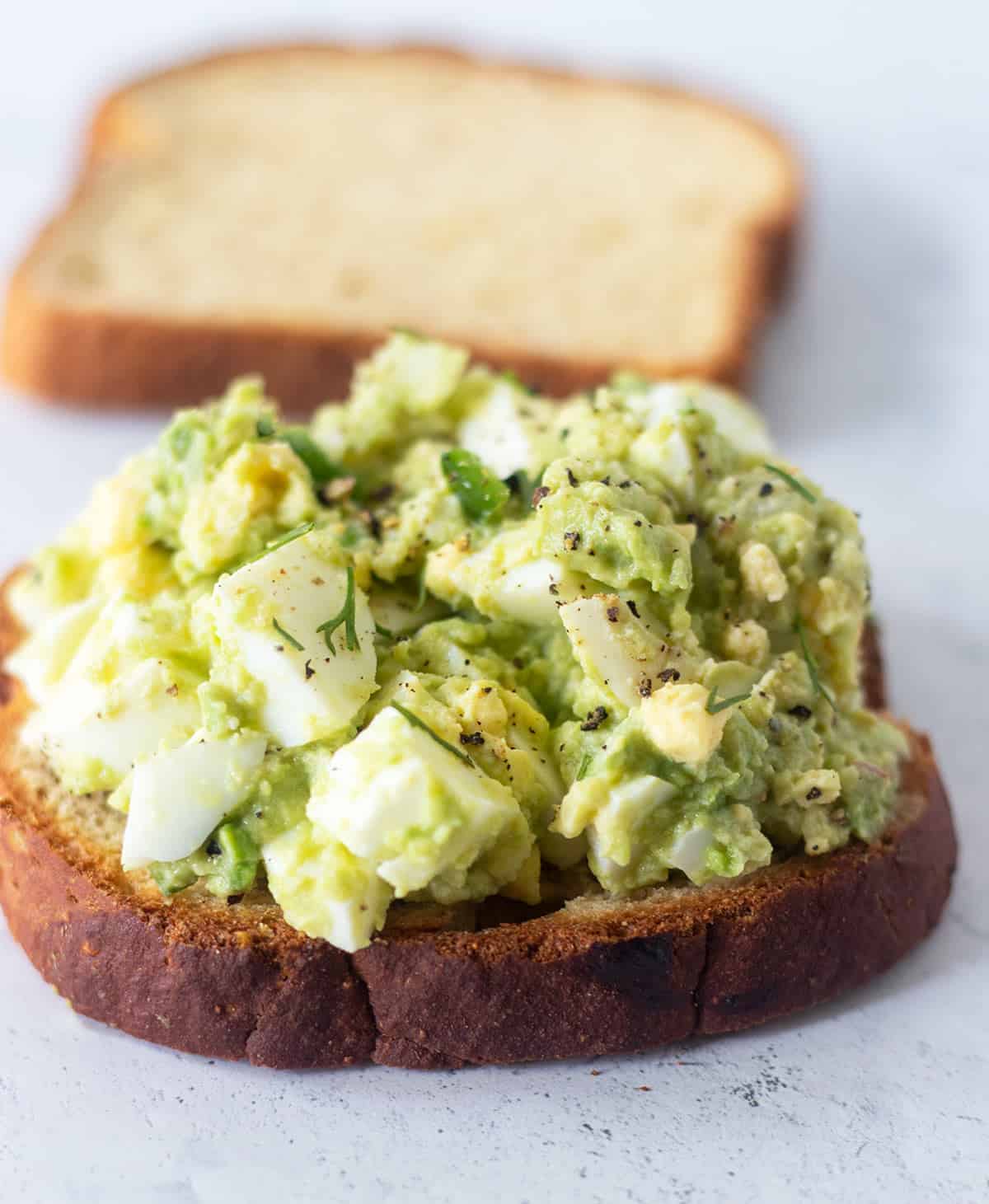 Avocado egg salad topped on a slice of bread with the other slice of bread in the background.