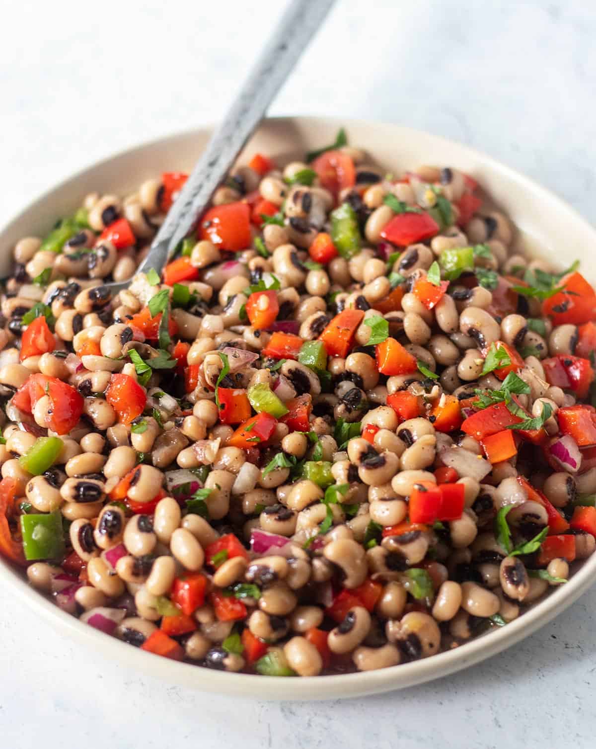 Black-eyed pea salad in a white salad dish with a silver spoon for serving.
